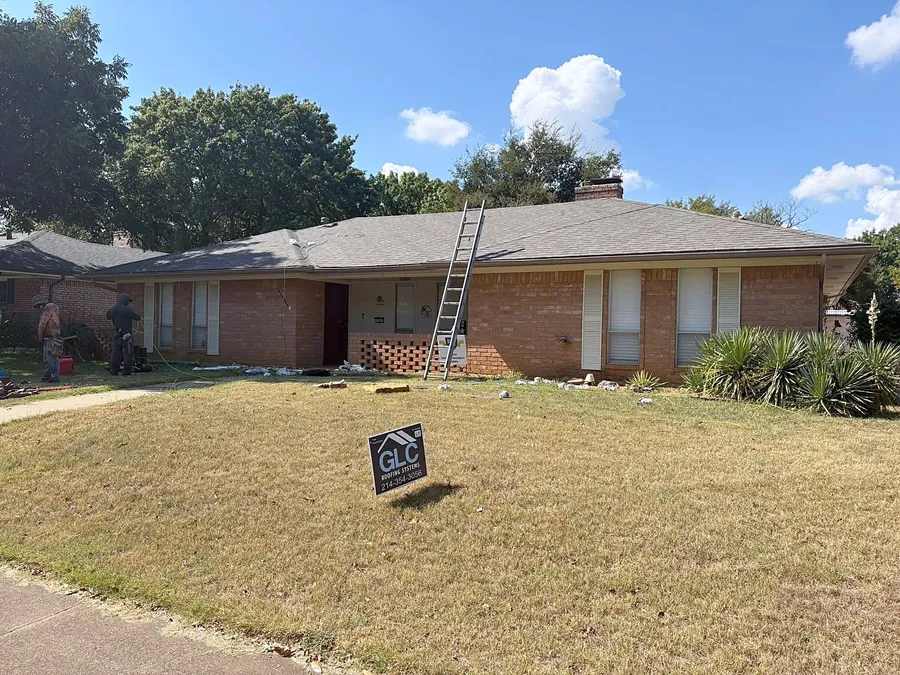 A ladder against a brick ranch home with the GLC crew at work and the GLC sign on the lawn