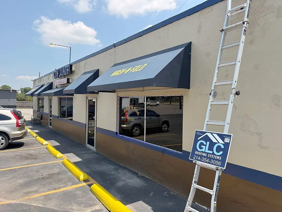 A strip of storefronts with a ladder up to the roof and the GLC Roofing Systems sign
