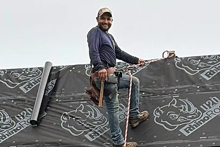 A member of the GLC crew, roped in and smiling, on a roof laid with new underlayment