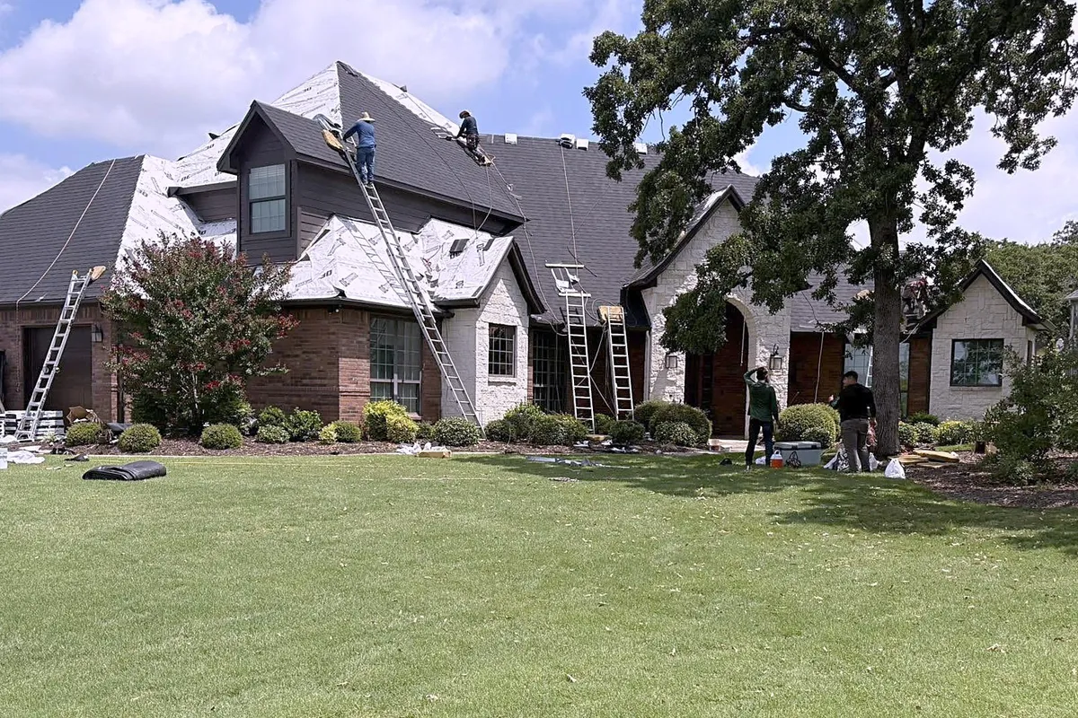 The GLC crew on ladders and on the roof, re-roofing a large brick and stone home