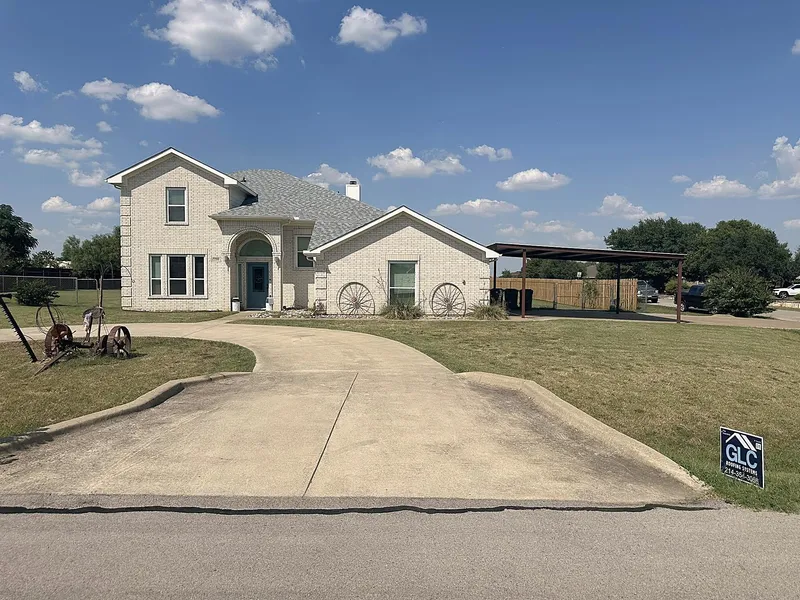 A white brick two-story home with a new gray shingle roof and the GLC sign by the drive