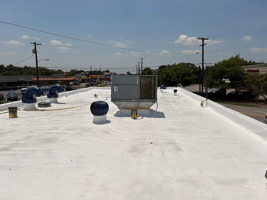 A white coated flat roof on a row of storefronts, with turbine vents and a rooftop unit